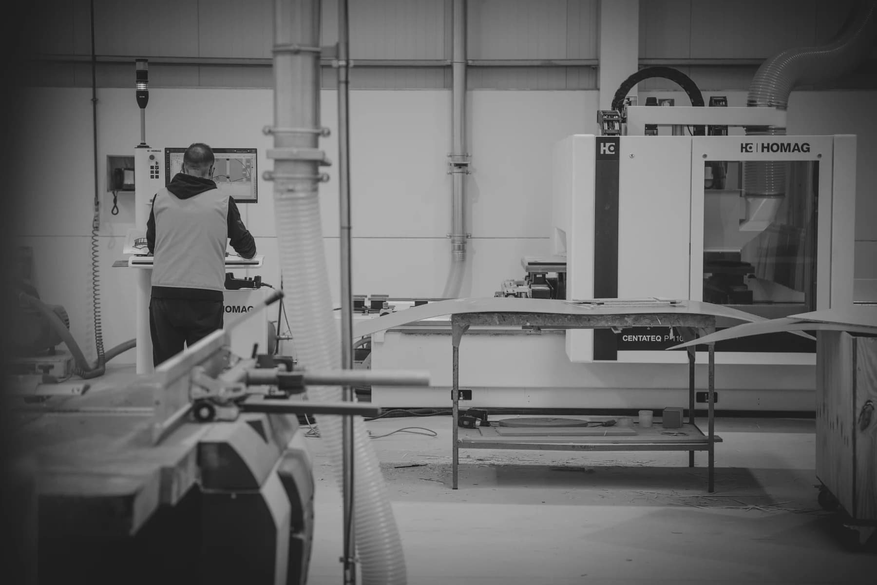 An ELBRA craftsperson operating woodworking machinery in the atelier, photographed in black and white